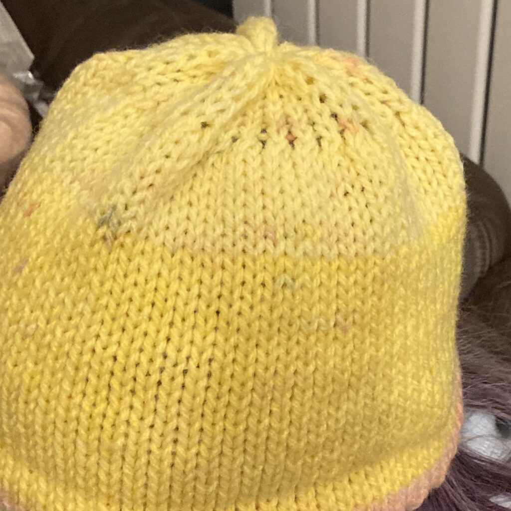 A photograph of the yellow hat version showing how the crown looks when the tension dial is decreased every 2 rows when the crown has alternating needles in non working posiition