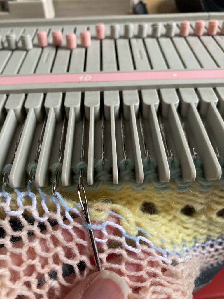 photo shows the first row in the finer yarn being transfered using a single pronged transfer tool onto the stitches already on the knitting machine